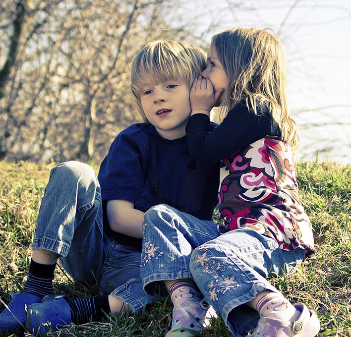 A girl whispering to a boy in a park